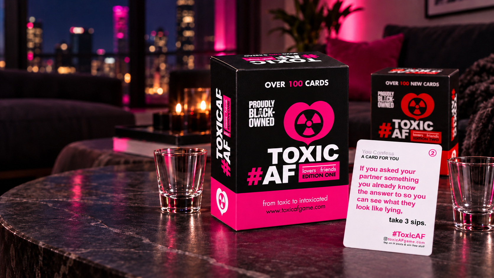 Pink Toxic AF Edition One and red Edition Two boxes with a white game card and shot glasses on a coffee table in a modern condo